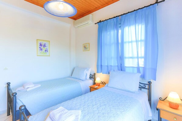 A bedroom with two beds, a wooden ceiling, and a window with blue curtains.