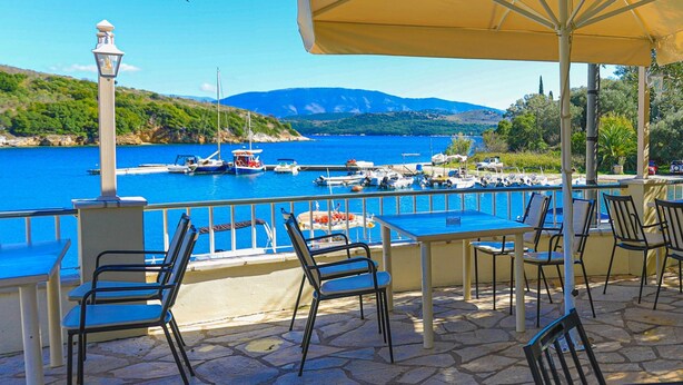 A terrace with stone flooring, outdoor seating, and a view of a body of water with boats. - Theophilos 2 in (Corfu)