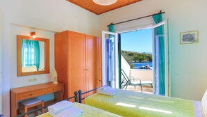 A room with two beds, a wooden wardrobe, a desk, and a mirror. There is a view of the sea through an open door. - Theophilos 1 in (Corfu)