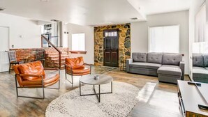 Ein geräumiger Wohnbereich mit Treppe, Steinwand und grauem Sofa.