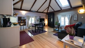 A spacious living area with a dining table, a sofa, and a kitchen in the background.