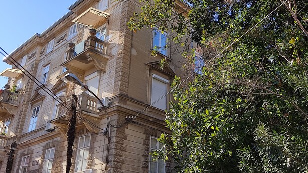 A multi-story building with balconies, a covered entrance, and a tree in the foreground.