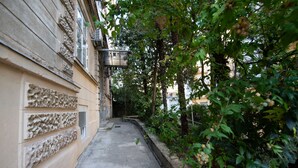A narrow alleyway with a building on one side and a tree-lined path on the other.
