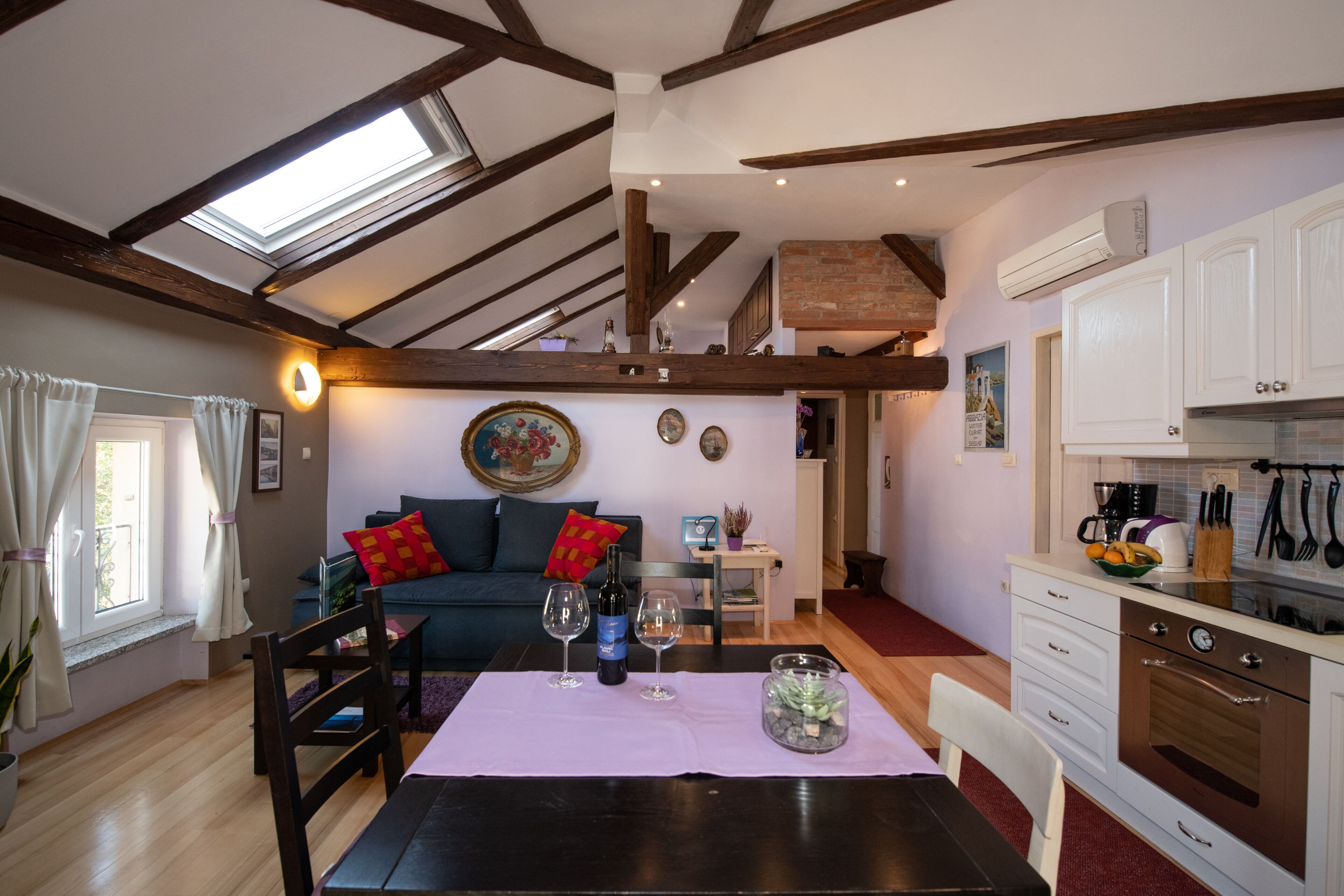 Una sala de estar acogedora con una mesa de comedor, un sofá con cojines, una zona de cocina con armarios y electrodomésticos, y un tragaluz.