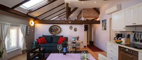 Una sala de estar acogedora con una mesa de comedor, un sofá con cojines, una zona de cocina con armarios y electrodomésticos, y un tragaluz.
