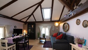 A cozy living room with a dining area, wooden beams, a sofa, and a table with chairs.