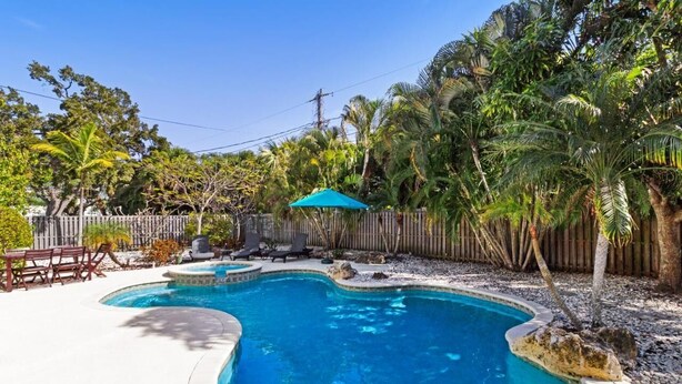 A swimming pool with a wooden deck, lounge chairs, and a blue umbrella.