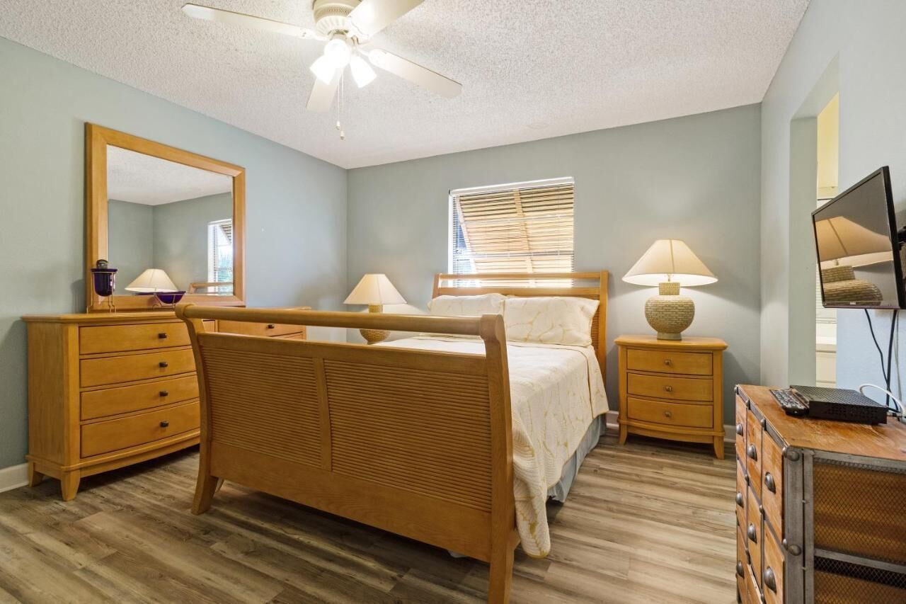Een slaapkamer met een houten bed, een plafondventilator, een raam met zonwering en een televisie op een dressoir.