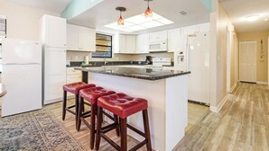 A modern kitchen with white cabinets, a central island with stools, and pendant lighting.