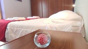A hotel room with a wooden bed, a red blanket, and a glass bowl with a red object on a wooden table.