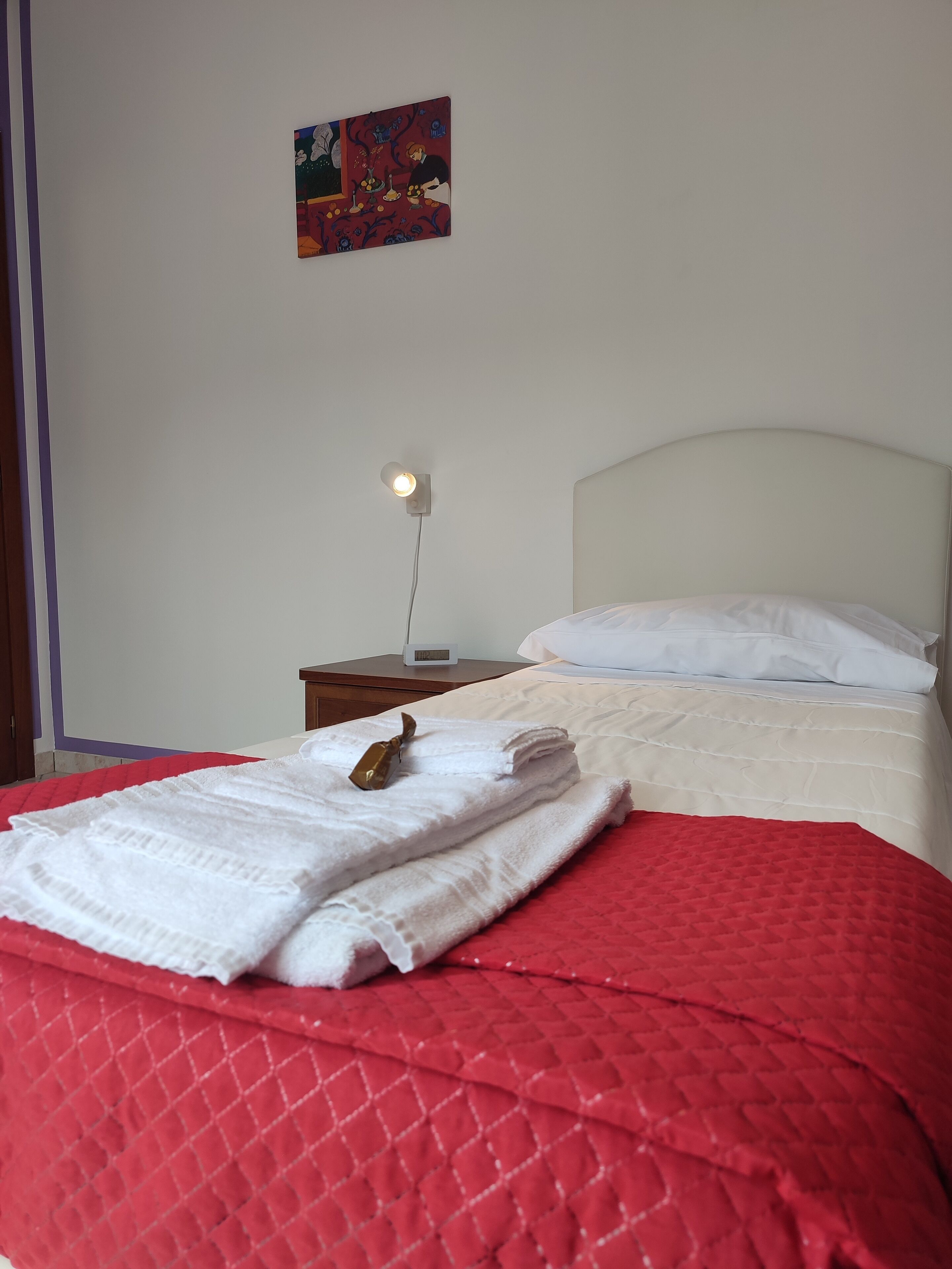 A neatly made bed with a red quilt, white pillows, and a folded towel on the side.