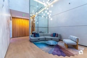 A modern interior with a sectional sofa, a round coffee table, and a minimalist chair. - Cityscape Balcony with Pool, Gym & Dining (Miami)