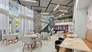 A modern restaurant with multiple dining areas, a staircase, and a view of the outdoors. - Rooftop Pool & Ocean Views Near Bayside (Miami)