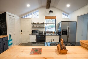A kitchen with a black countertop, white cabinets, a stainless steel refrigerator, a microwave, and a sink. - Cozy, Pet Friendly Home Steps from GFL (Quitman)