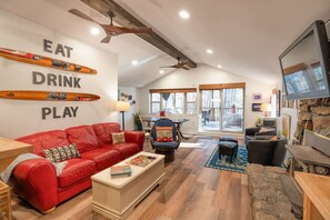 A spacious living room with a red leather couch, a wooden coffee table, and a television. There are skis mounted on the wall, and a ceiling fan is visible.