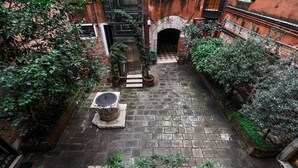 An outdoor courtyard with a brick floor, potted plants, a stone bench, and a metal door. - Luxury apartment, 100m from Piazza San Marco, Venice (Venezia)