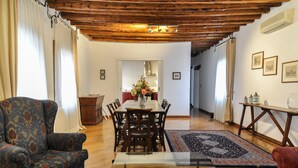A spacious living room with a wooden ceiling, a dining area with a table and chairs, and a coffee table with decorative items. - Luxury apartment, 100m from Piazza San Marco, Venice (Venezia)
