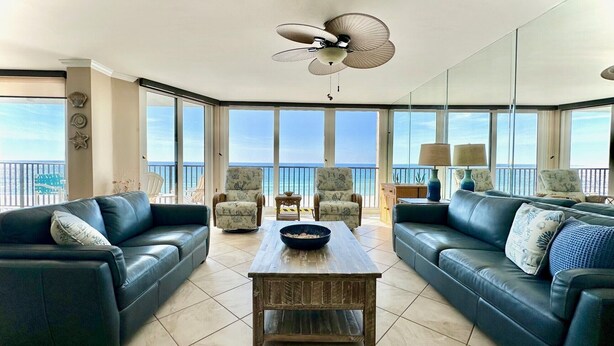 A spacious living room with a large window overlooking the ocean, furnished with leather sofas, armchairs, and a wooden coffee table. - Pelican Walk 406 - BEST VIEW! Free Beach Chairs! (PANAMA CITY Beach)