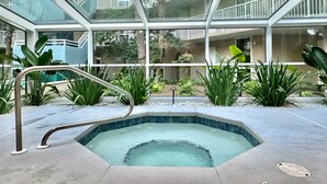 A modern indoor pool area with glass railings, surrounded by tropical plants and a clear view of the surrounding buildings. - Pelican Walk 406 - BEST VIEW! Free Beach Chairs! (PANAMA CITY Beach)