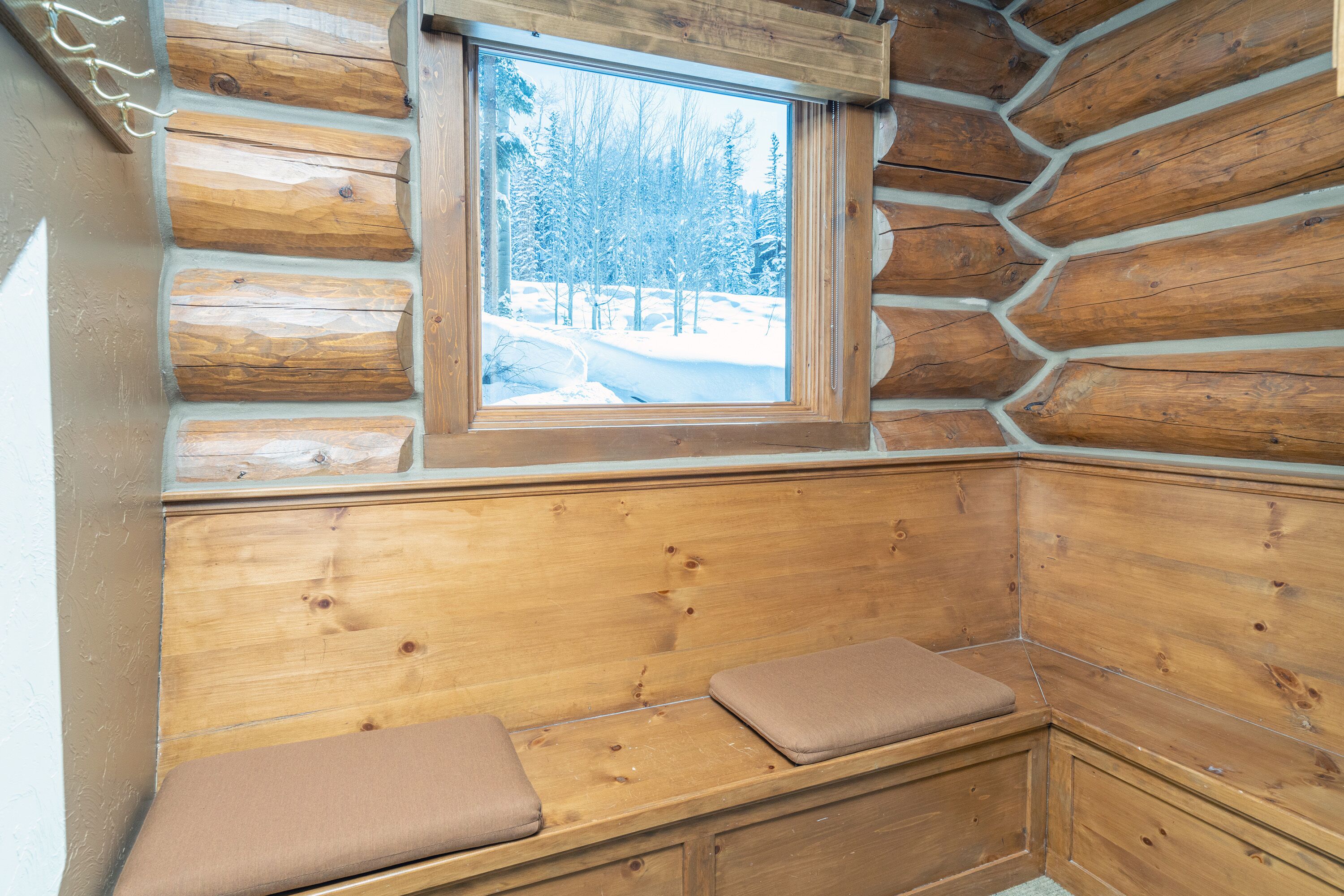 Ein Holzblockhaus-Innenraum mit einer Bank und einem Fenster mit Blick auf eine verschneite Landschaft.