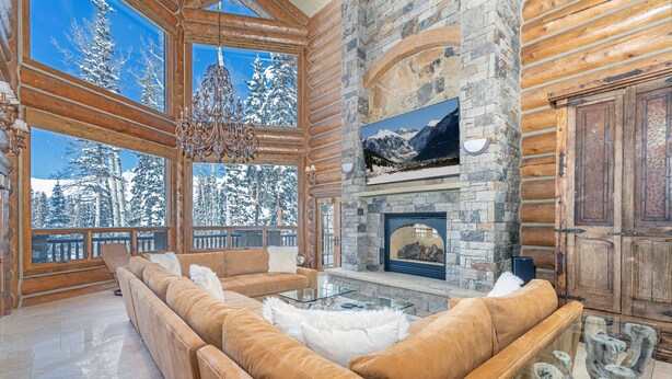 A log cabin interior with a stone fireplace, leather sofas, and large windows overlooking a snowy landscape. - BEARPAW MANOR- A Magnificent Ski-In/Ski-Out Mountain Village Chalet (Mountain Village)