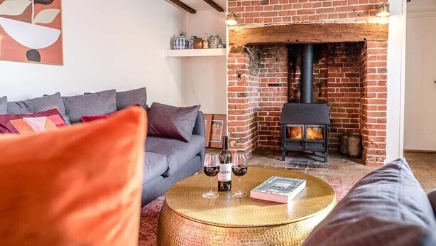 A cozy living room with a brick fireplace, a sofa, and a round coffee table with a book and glasses. - Solebay House, Tunstall (Woodbridge)