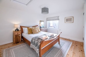 Une chambre à coucher avec un lit en bois, une table de chevet, une fenêtre donnant sur un beau paysage et un luminaire au plafond.