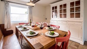 A dining area with a wooden table set for a meal, red chairs, and a white cabinet with glass doors. - Solebay House, Tunstall (Woodbridge)