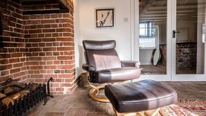 A cozy room with a brick fireplace, a leather armchair, and a matching ottoman. - Solebay House, Tunstall (Woodbridge)