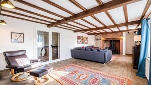 A spacious living room with a leather sofa, a leather chair, a patterned rug, and exposed wooden beams on the ceiling. - Solebay House, Tunstall (Woodbridge)