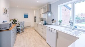 A modern kitchen with white cabinets, a built-in oven, and a large window providing a view of the outside. - Little Hotsie, Southwold (Southwold)