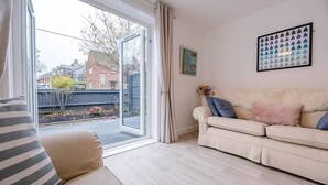 A living room with a sofa, a window with curtains, and a framed picture on the wall. - Little Hotsie, Southwold (Southwold)