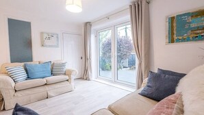 A modern living room with a beige sofa, a white armchair, and a large window with curtains. - Little Hotsie, Southwold (Southwold)