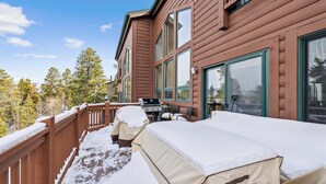 Une cabane en bois dotée d’une terrasse recouverte de neige, d’un barbecue et offrant une vue sur les arbres.