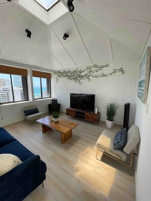 Un salon moderne avec un téléviseur à écran plat, une table basse en bois, un canapé bleu et un fauteuil blanc.