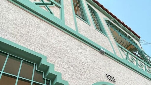 Un edificio con fachada de color claro, marcos de ventanas verdes y un balcón.