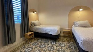 Una habitación con dos camas, piso estampado y ventana con cortinas.