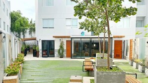 A courtyard with a central grassy area, benches, planters, and a building with large windows and a door. - w* | 1BR near Central Restaurant in Barranco (Barranco)