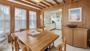 Een houten interieur met een eettafel, stoelen, een plafondventilator en een keukenruimte zichtbaar door een open doorgang.