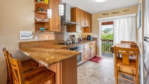 A modern kitchen with granite countertops, wooden cabinets, stainless steel appliances, and pendant lighting. - Hale Moana E21, Coconut Grove Views, Walk to Kapaa Town and Beach (Kapaa)