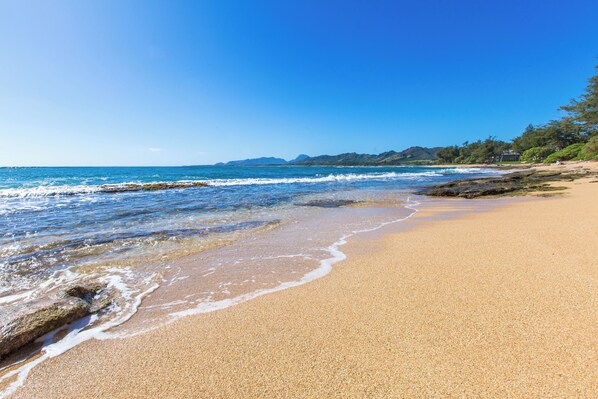 A beach with clear blue water, sandy shore, and distant mountains.