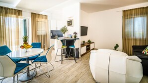A modern living room with a round dining table, blue chairs, a white sofa, and a flat-screen TV mounted on the wall. - Villa Dana with Private Pool (Novalja)