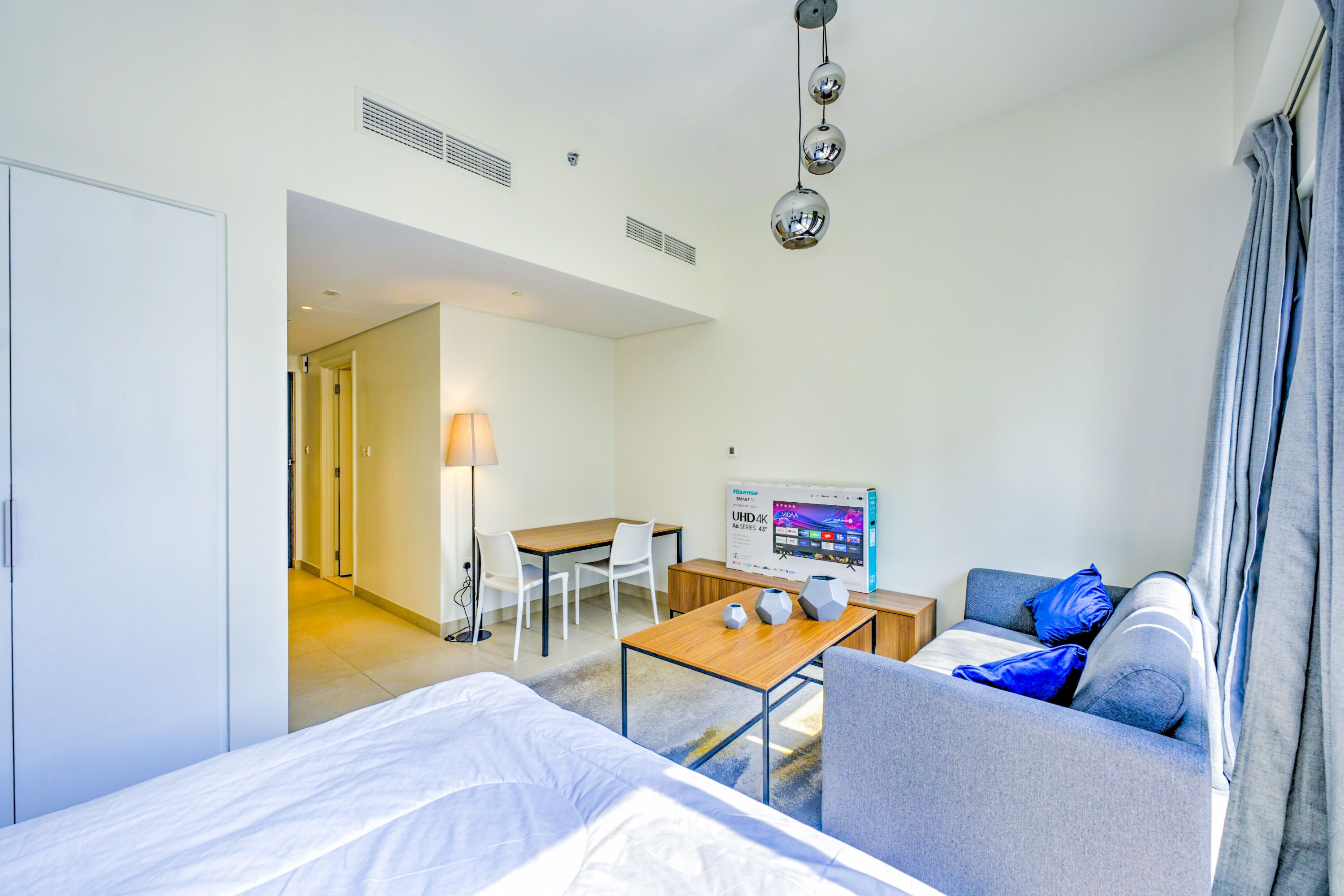 Ein Hotelzimmer mit Bett, Sofa, Schreibtisch und Stuhl. Eine Lampe, ein Fernseher und ein Plakat sind an der Wand angebracht.