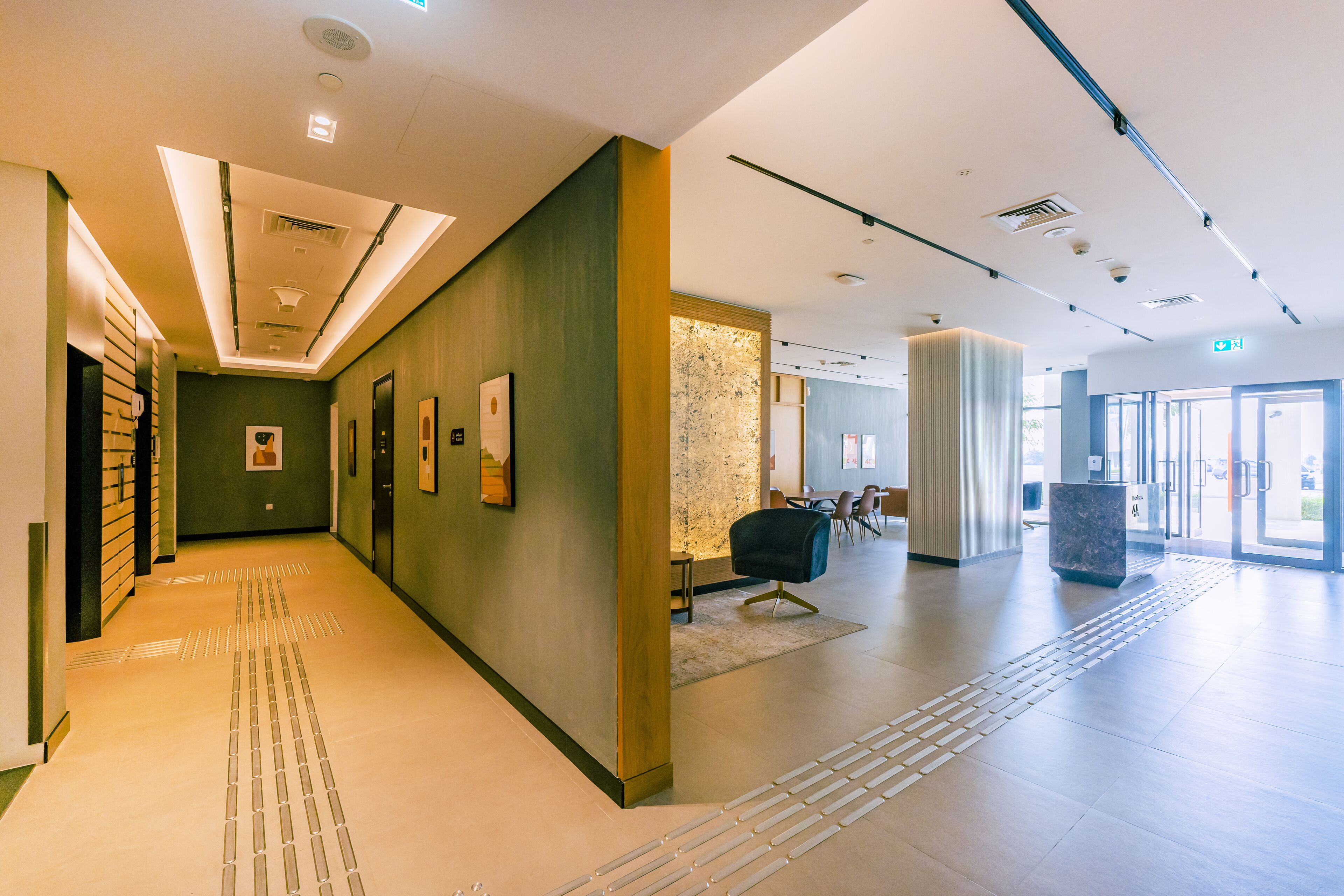 A modern hotel lobby with a long corridor, a reception desk, and a waiting area with chairs.