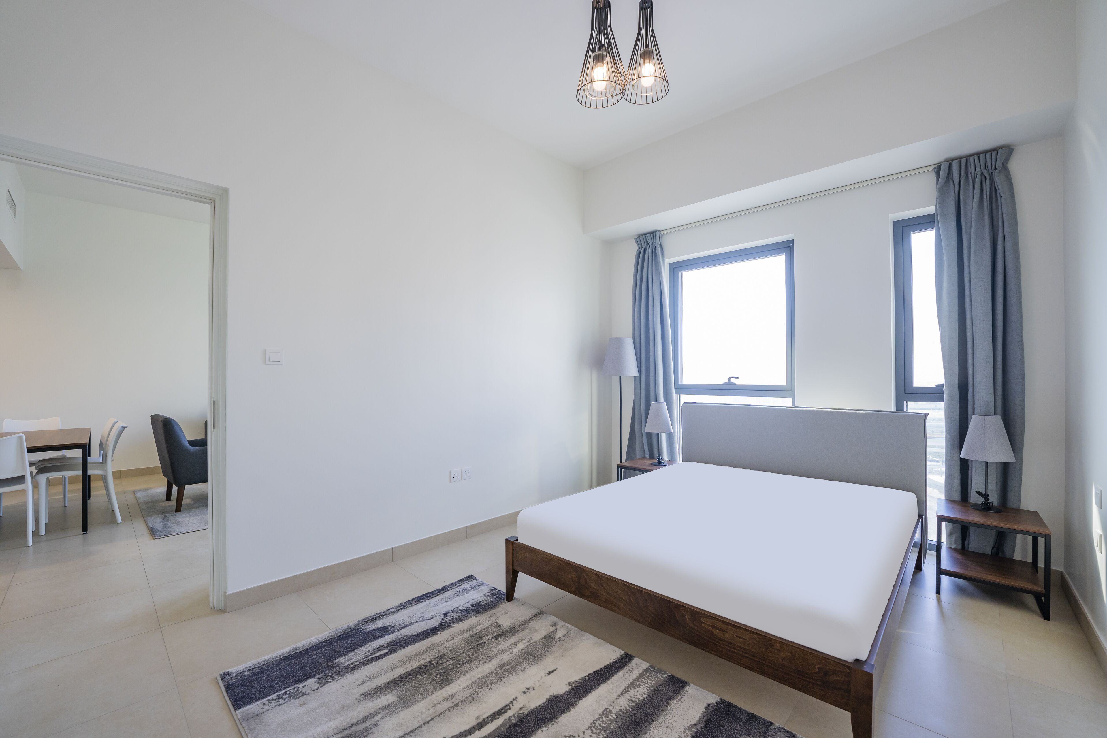 A modern bedroom with a large bed, a desk, and a chair, a window with curtains, and a hanging light fixture.
