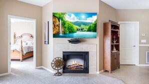 A living room with a fireplace, a television mounted above it, and a bed in the adjacent room.