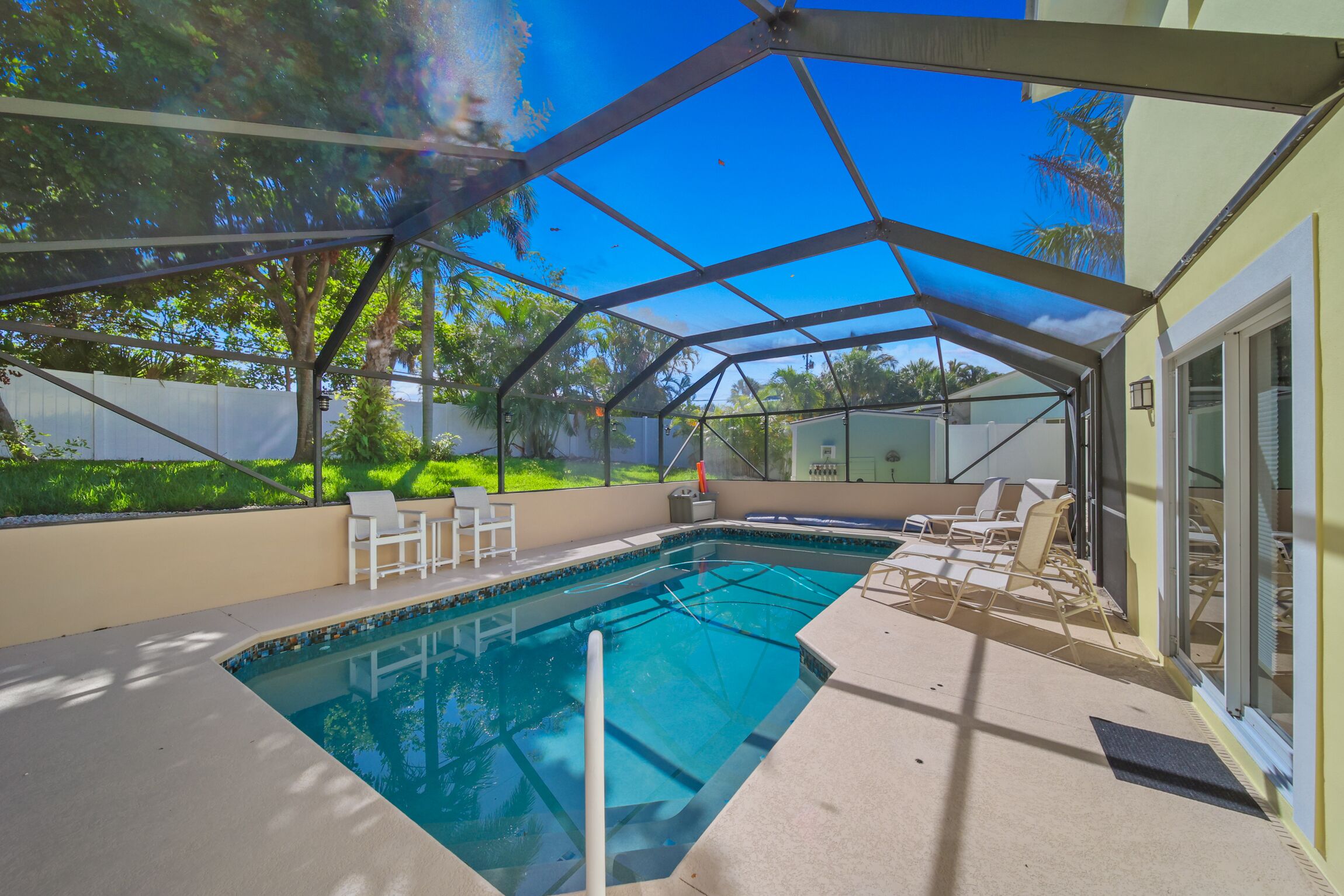 A covered outdoor swimming pool with lounge chairs and a glass enclosure.