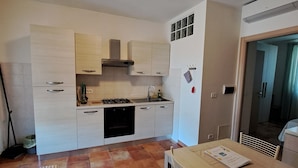 A compact kitchen with white cabinets, a gas stove, and a dining area with a table and chairs. - Agriturismo La Tortorella (Grosseto)