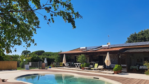 A swimming pool with a wooden deck, outdoor seating, and solar panels on the roof. - Agriturismo La Tortorella (Grosseto)
