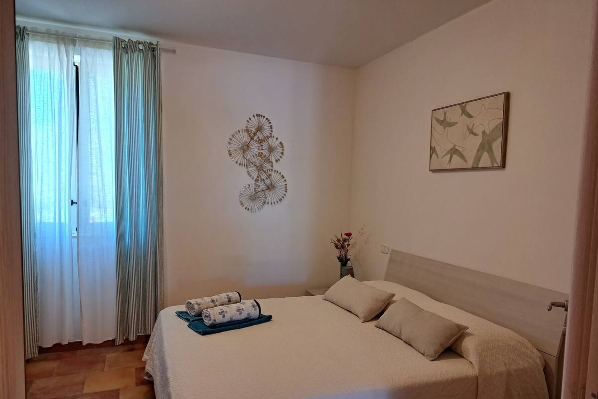 Une chambre à coucher avec un lit, un élément de décoration murale, un tableau encadré et une fenêtre avec des rideaux.